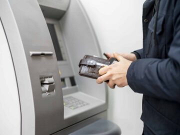 persons hand hold a wallet with cash and withdraw some money in atm